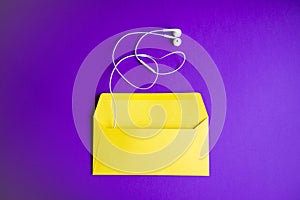 Yellow headphones on envelopment on purple background.