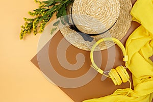 Yellow headphones with tropic leaves, straw hat on brown background. Trendy fashion accessories. Flat lay, close up. Summer,
