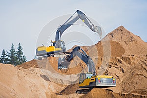 Yellow heavy excavator and bulldozer excavating sand and working during road works, unloading sand and road metal