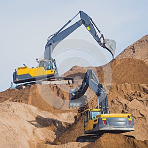 Yellow heavy excavator and bulldozer excavating sand and working during road works, unloading sand and road metal during construct