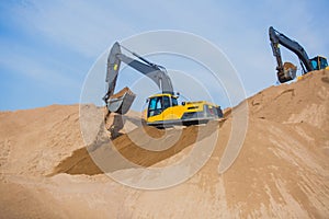 Yellow heavy excavator and bulldozer excavating sand and working during road works, unloading sand and road metal during construct