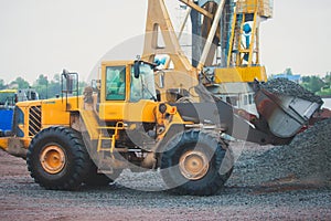 Yellow heavy excavator and bulldozer excavating sand and working during road works, unloading sand and road metal during construct