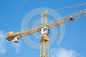 Yellow hoisting crane on blue sky background with clouds