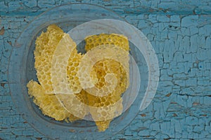 Yellow honeycomb in the clear plastic dish on the old wooden background painted paint