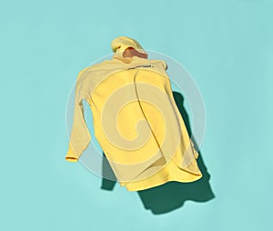 Yellow hoodie jersey sweater is flying thrown in the air, falling down from sky over blue background. In motion