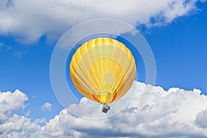 Yellow hot air balloon is suspended in the sky, with wispy white clouds in the background