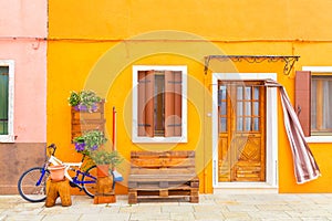 Yellow house with flowers, bench and a bicycle. Colorful houses in Burano island near Venice, Italy. Venice postcard. Famous place