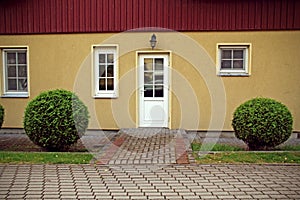 Yellow house front door with red roof and neat bushes