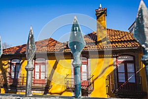 a yellow house with a metal hedge and a seagull on the chimney