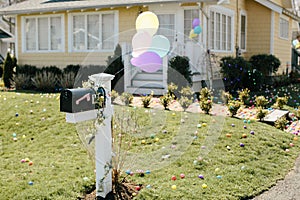 Yellow house with pastel balloons on mailbox with easter eggs on the lawn