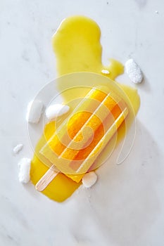 Yellow Icecream lolly pop over marble light background with ice and juice, flat lay