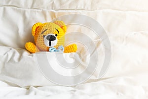 Yellow ill teddy bear lying in bed on white background.
