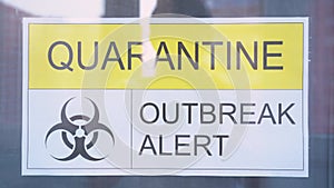 Yellow inscription with black warning printed word QUARANTINE OUTBREAK ALERT, sign with radiation symbol glued to window glass