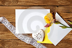 Yellow iris flower, white sheet of paper, heart and lace ribbon on a wooden background. Flat layout with space for text