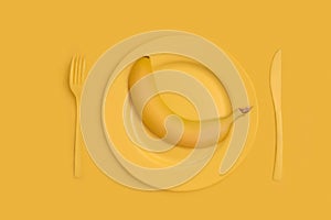 Yellow juicy banana on top of a yellow plate, knife and fork. On yellow background. The view from the top