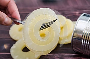 Yellow juicy pineapple ring on a fork against the background of a tin can. Caramelized canned pineapple. Raw food diet. Close-up p