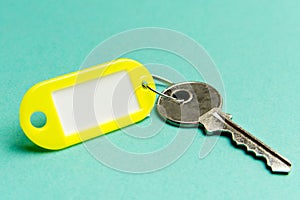 Yellow key tag on a turquoise textured cardboard background.The concept of rent, selling. Template. Trend colors