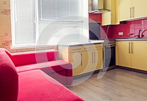 Yellow kitchen with cupboards, window, laminate and red soft couch