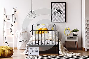 Yellow knot pillow on single metal bed in bright bedroom interior with white scandinavian ladder, paper bag with toys and