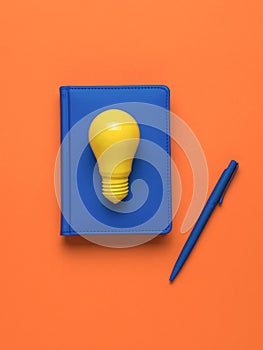 A yellow lamp, a notebook with a pen on an orange background. Flat lay