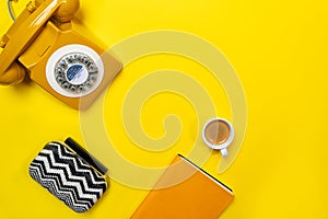 Yellow layout with retro rotary telephone, cup of coffee, bag and notebook.