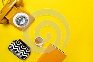 Yellow layout with retro rotary telephone, cup of coffee, bag and notebook.