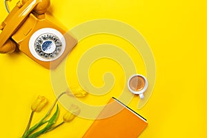 Yellow layout with retro rotary telephone, cup of coffee, flowers and notebook.