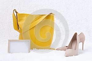 Yellow leather bag and high-heeled shoes on a white fur background. Next to it is a frame for text. A place to designate