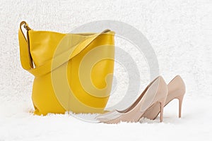Yellow leather bag and high-heeled shoes on a white fur background. Stylish and fashionable shop window