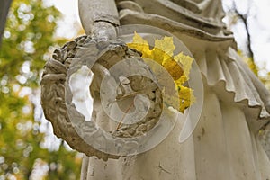 Yellow leaves lie on the laurel wreathn in hand of the sculpture, autumn city park, sunny day