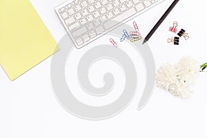 Yellow legal pad, keyboard, paper clips, a pencil and a chrysanthemum flower on a white background. Flat lay concept of the workpl
