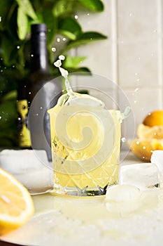 Yellow lemon Limoncello liqueur cocktail with splash drops at kitchen background.