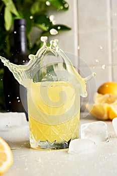 Yellow lemon Limoncello liqueur cocktail with splash drops at kitchen background.