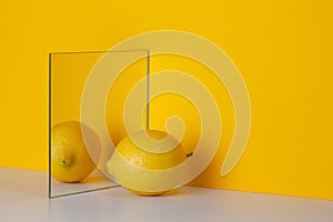 Yellow lemon is reflected in a mirror on a yellow background