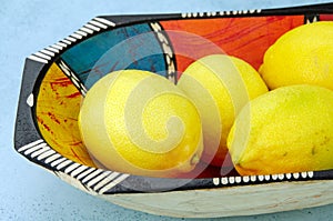 Yellow lemons in colourful wooden bowl
