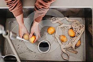 Yellow lemons are in net cotton shopping bag in sink. Washing fruits before using them. Local farm produce. Fresh seasonal food.