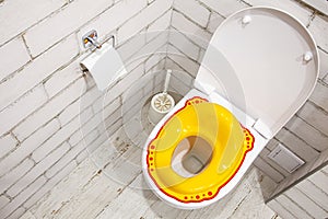 Yellow lid for toilet seat for children. How to accustom a child to the toilet. White bathroom. Copy space for text.