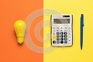 A yellow light bulb, a calculator and a blue pen on an orange and yellow background