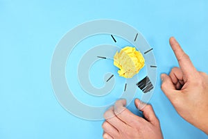 Yellow light bulb crumpled paper with hands in blue background. Bright ideas and new innovation concept. Flat lay