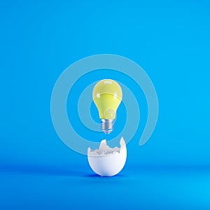 Yellow light bulb floating from white eggshell on blue background.