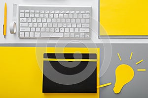 Yellow light bulb idea metaphor on desktop with keyboard pc computer and suppliers in workspace on gray table background