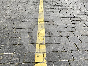 Yellow line in the center of grey brick of road. Concrete footpath arrangement.