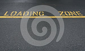 Yellow line and loading zone text on an asphalt street