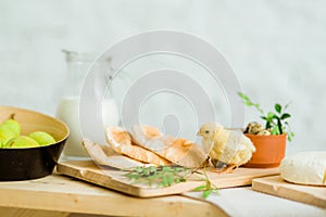 Yellow little chicken on the table with easter decoration, bread, cheese and herbs.