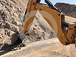 Yellow loader backhoe digs a trench during road construction works. Earthmoving, excavations, digging on the rocky soils