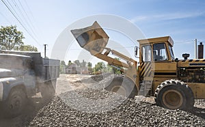 Yellow loader delivering stone gravel into truck during road construction works. The stones for the road. Unloading