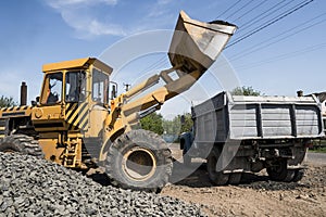 Yellow loader delivering stone gravel into truck during road construction works. The stones for the road. Unloading