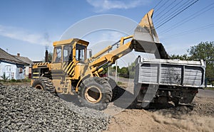 Yellow loader delivering stone gravel into truck during road construction works. The stones for the road. Unloading