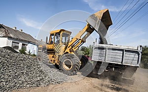 Yellow loader delivering stone gravel into truck during road construction works. The stones for the road. Unloading