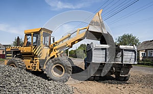 Yellow loader delivering stone gravel into truck during road construction works. The stones for the road. Unloading